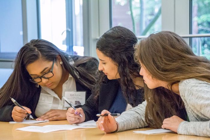 three students confer with pens in hand